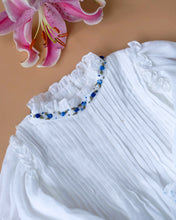 Load image into Gallery viewer, The pintuck detailing across the bust and ruffles running across the neckline in classic white palette kept upon a peach background with a leaf aside.
