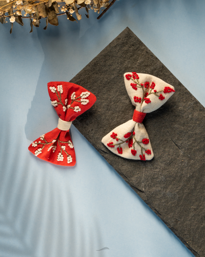 A beautiful Christmas red and white floral hair clips for kidswear kept upon grey sheet and also on blue background with some dried flowers aside.