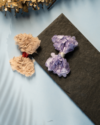 A beautiful beige color and rose flower purple hair accessories kept upon a grey sheet with dry leaves aside.