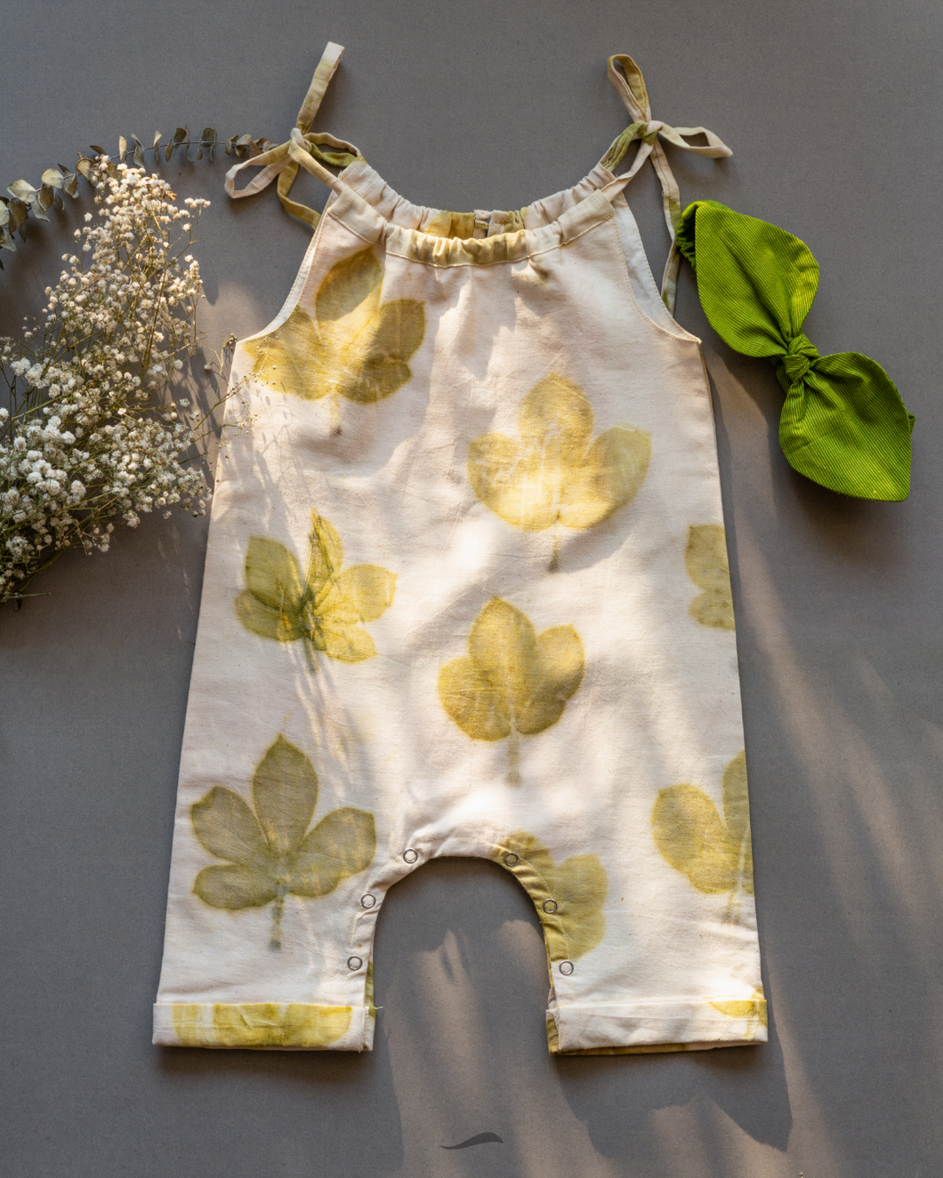 A cute baby girl dress made of eco-printed Indian maple leaves on it along with matching hair accessory and some flower aside.