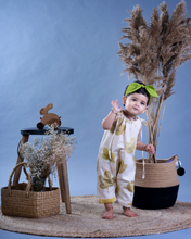 Load image into Gallery viewer, A baby girl wearing a jumpsuit with matching hair accessories with some artificial plants and wooden pots and with some rabbit toys and a flower basket aside.
