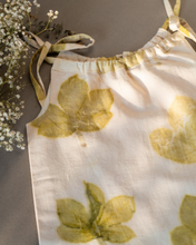 Load image into Gallery viewer, A cute baby girl dress made of eco-printed Indian maple leaves on it along with some flower aside.
