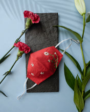 Load image into Gallery viewer, A red color organic cotton hand-embroidered adjustable face masks kept upon a grey sheet with some flowers aside.
