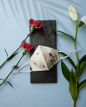 Load image into Gallery viewer, A white color organic cotton hand-embroidered adjustable face masks kept upon a grey sheet with some flowers aside.
