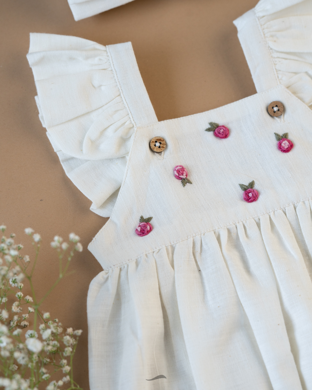 A cute romper with some flower embroidery on it with some flower aside.