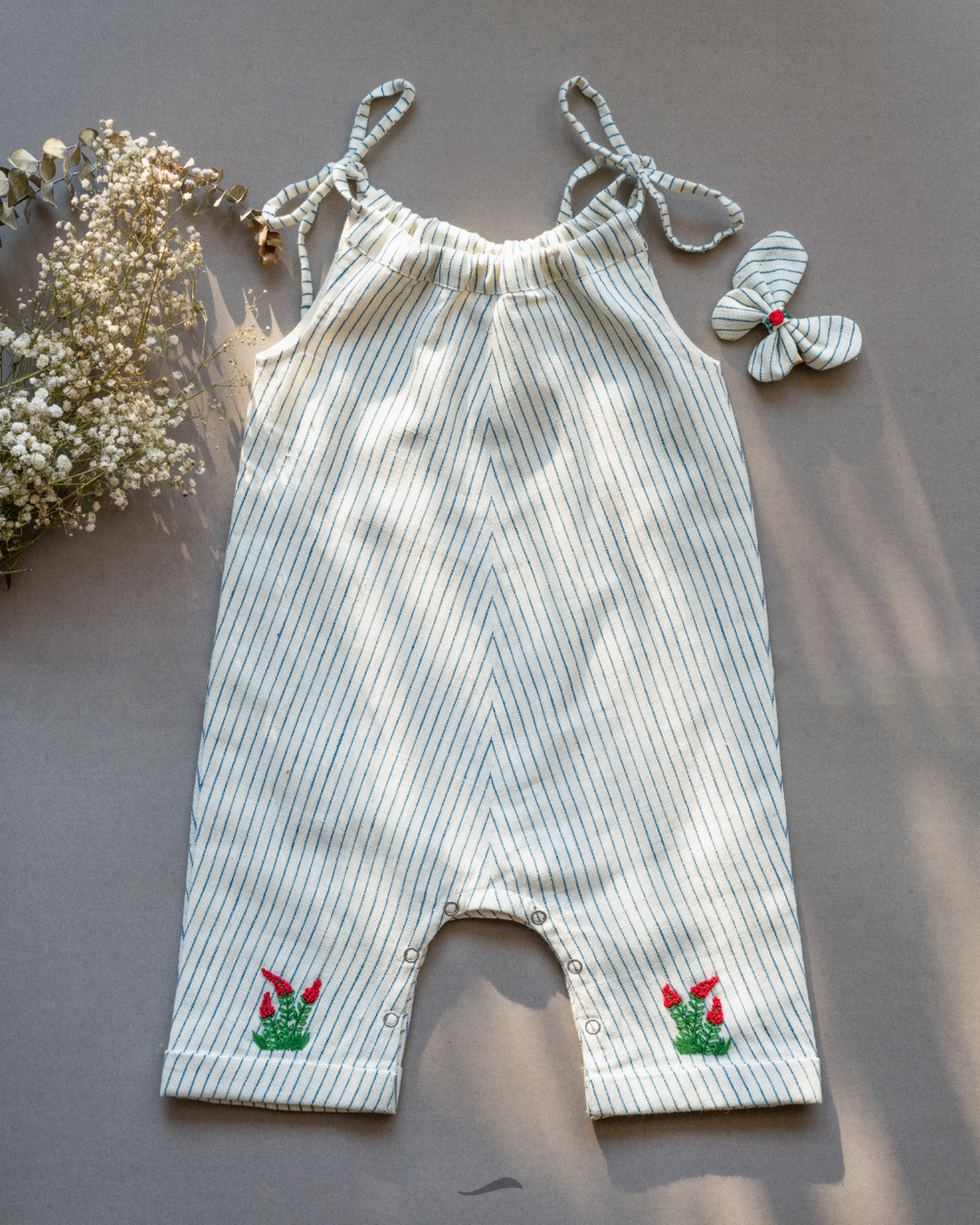 A cute baby girl dress along with matching hair accessory and some flower aside.